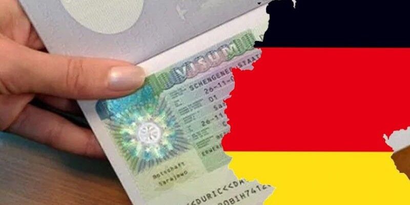 شخص يمسك بيده فيزا ألمانية - وعلم ألمانيا